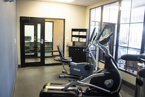 A fitness room with exercise equipment, a door leading to another room, and a window with a view.