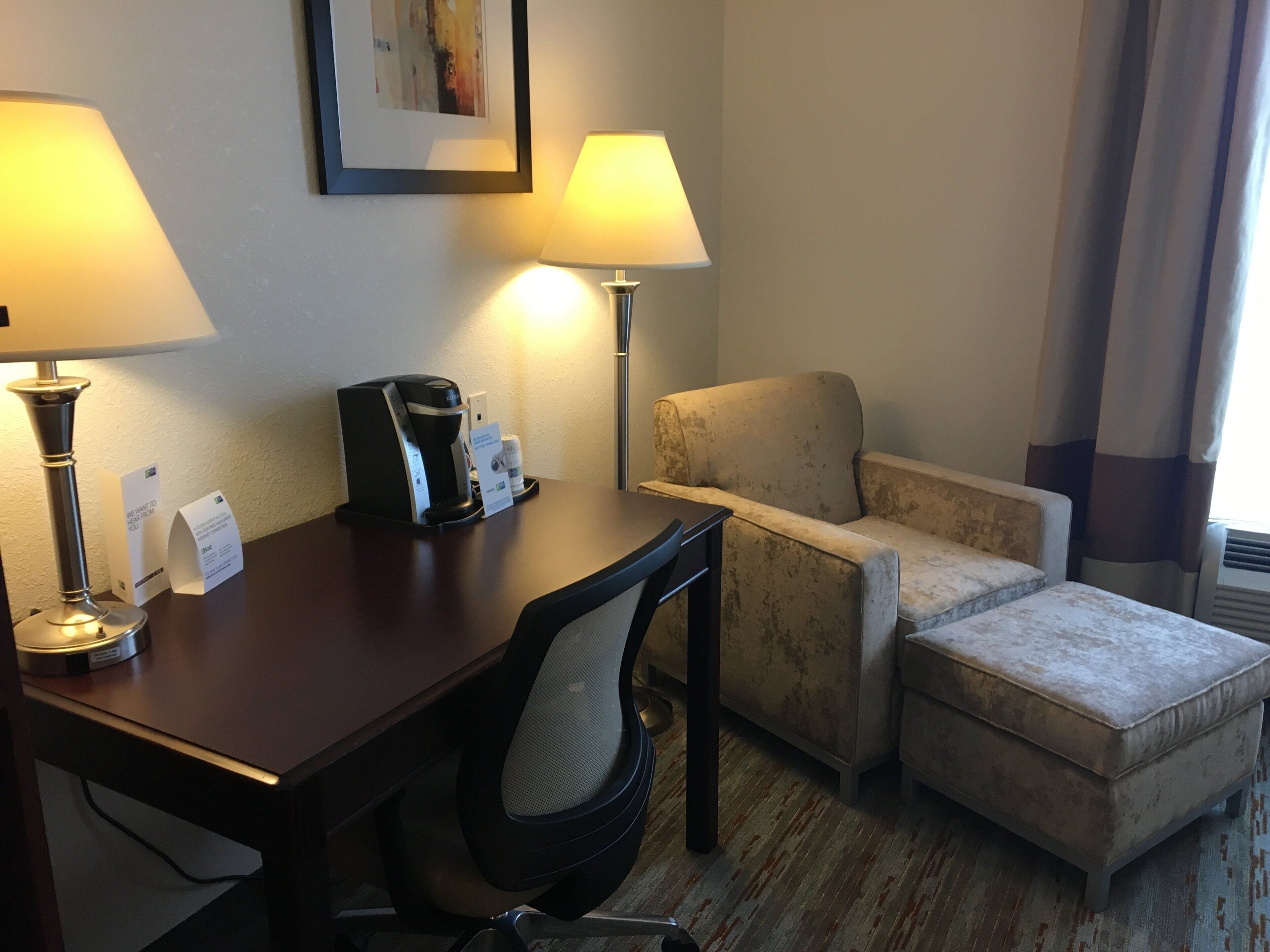 Une chambre d’hôtel équipée d’un bureau, de deux lampes, d’une machine à café, d’une chaise et d’un canapé.