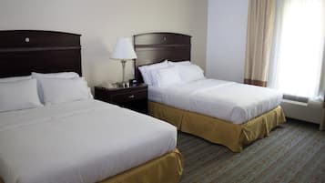 Two beds with white linens, a nightstand with a lamp, and a window with curtains.