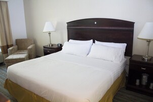 Una habitación de hotel con una cama grande, dos mesitas de noche, una silla y una lámpara.