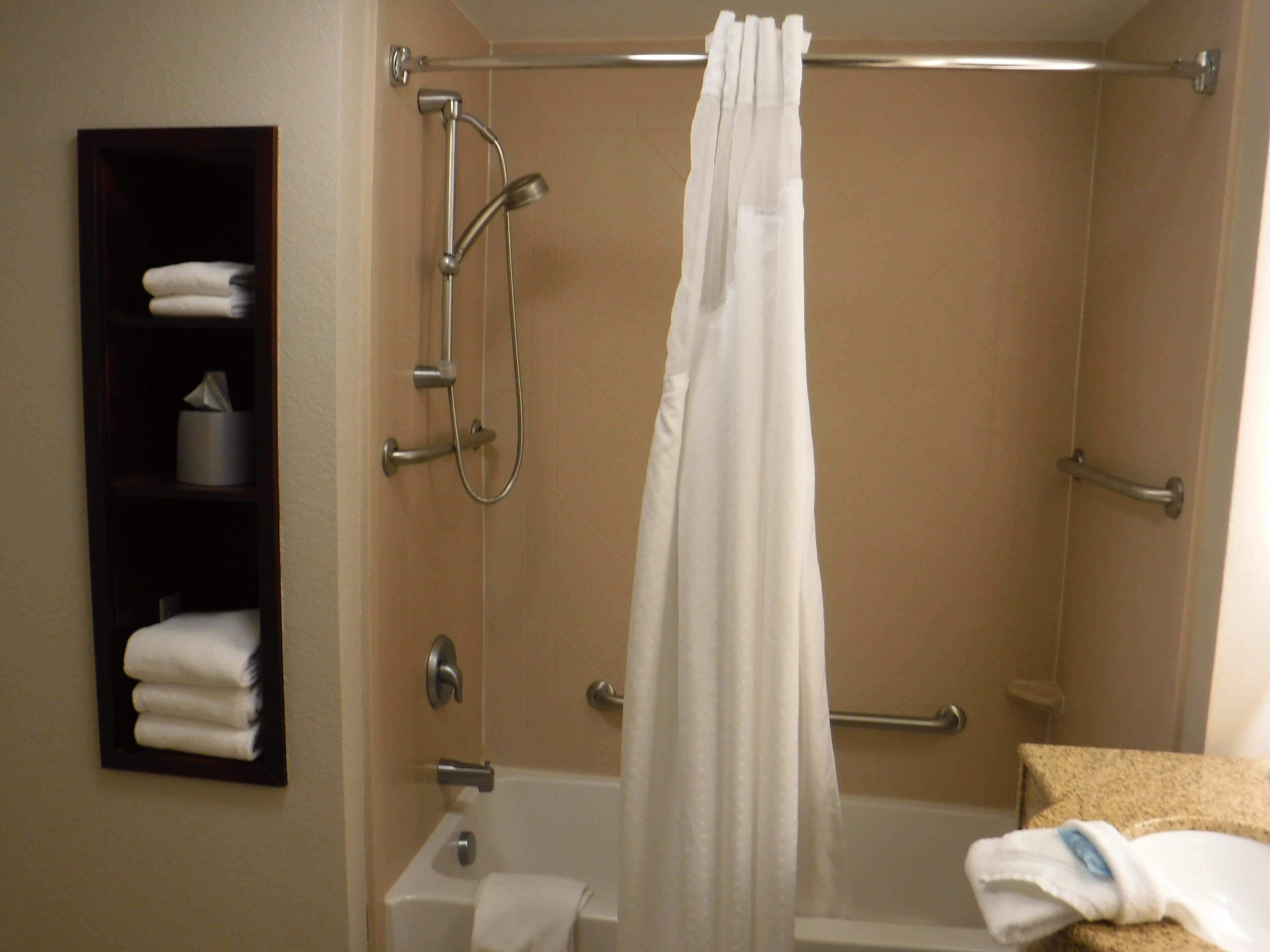 A shower with a curtain, a towel rack, and a shelf with towels.