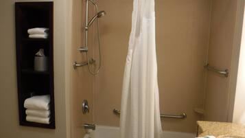 A shower with a curtain, a towel rack, and a shelf with towels.