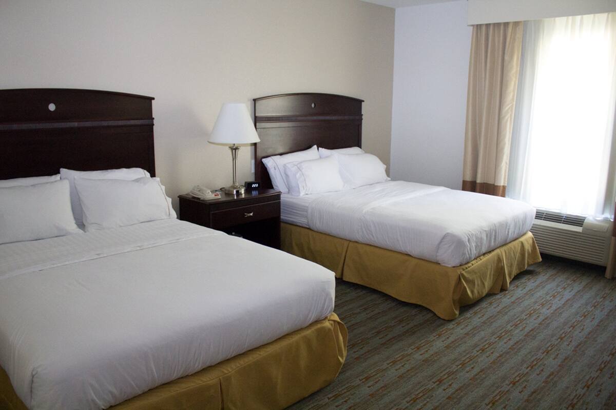 Two single beds with wooden headboards, a bedside table with a lamp, and a window with curtains.