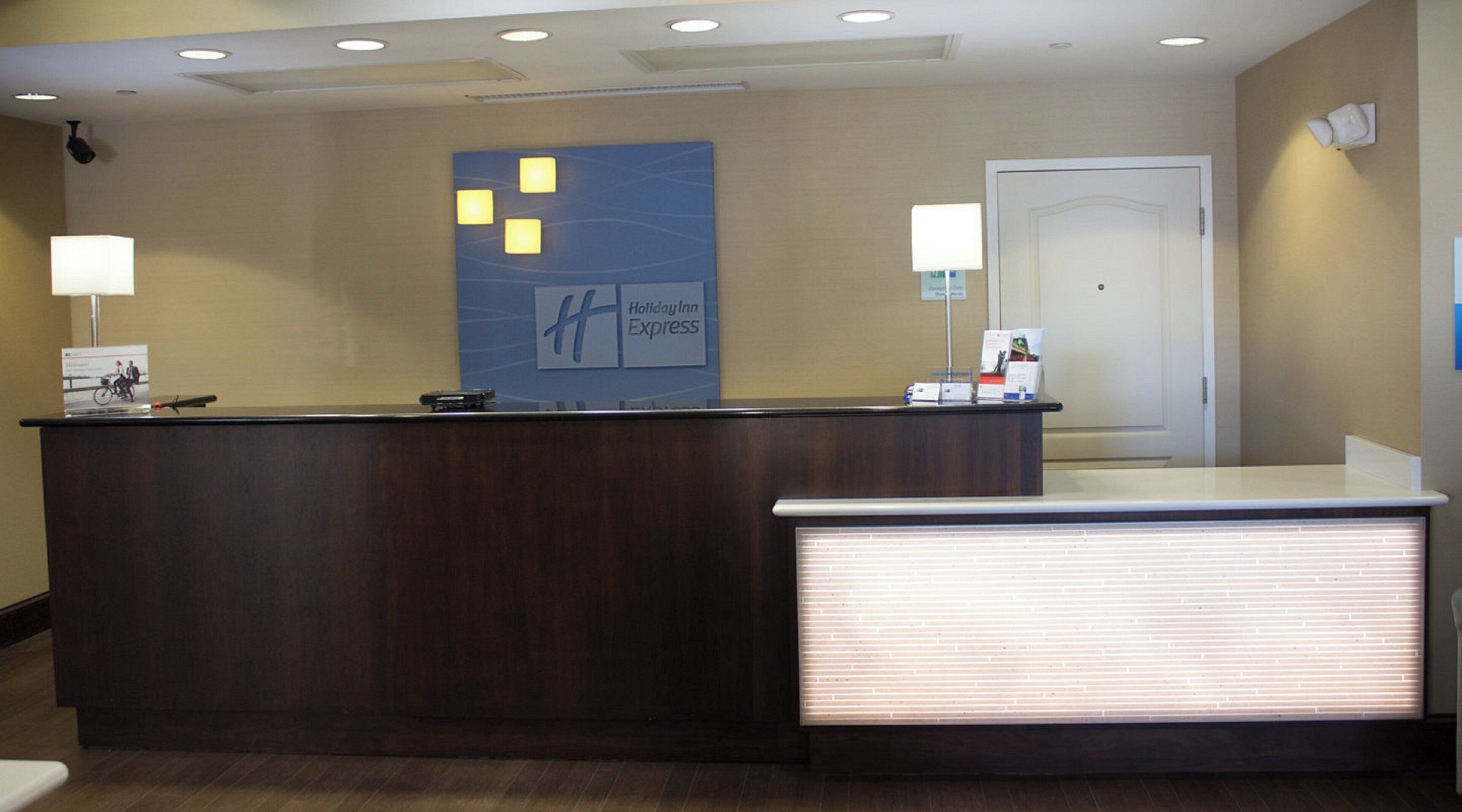 Un mostrador de recepción de hotel con una pantalla digital, un cartel de Holiday Inn Express y una puerta al fondo.