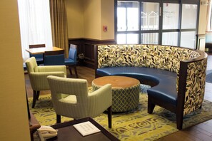 A seating area with a curved sofa, two armchairs, and a small round table with a telephone and a sign. - Holiday Inn Express West Jefferson by IHG (West Jefferson)