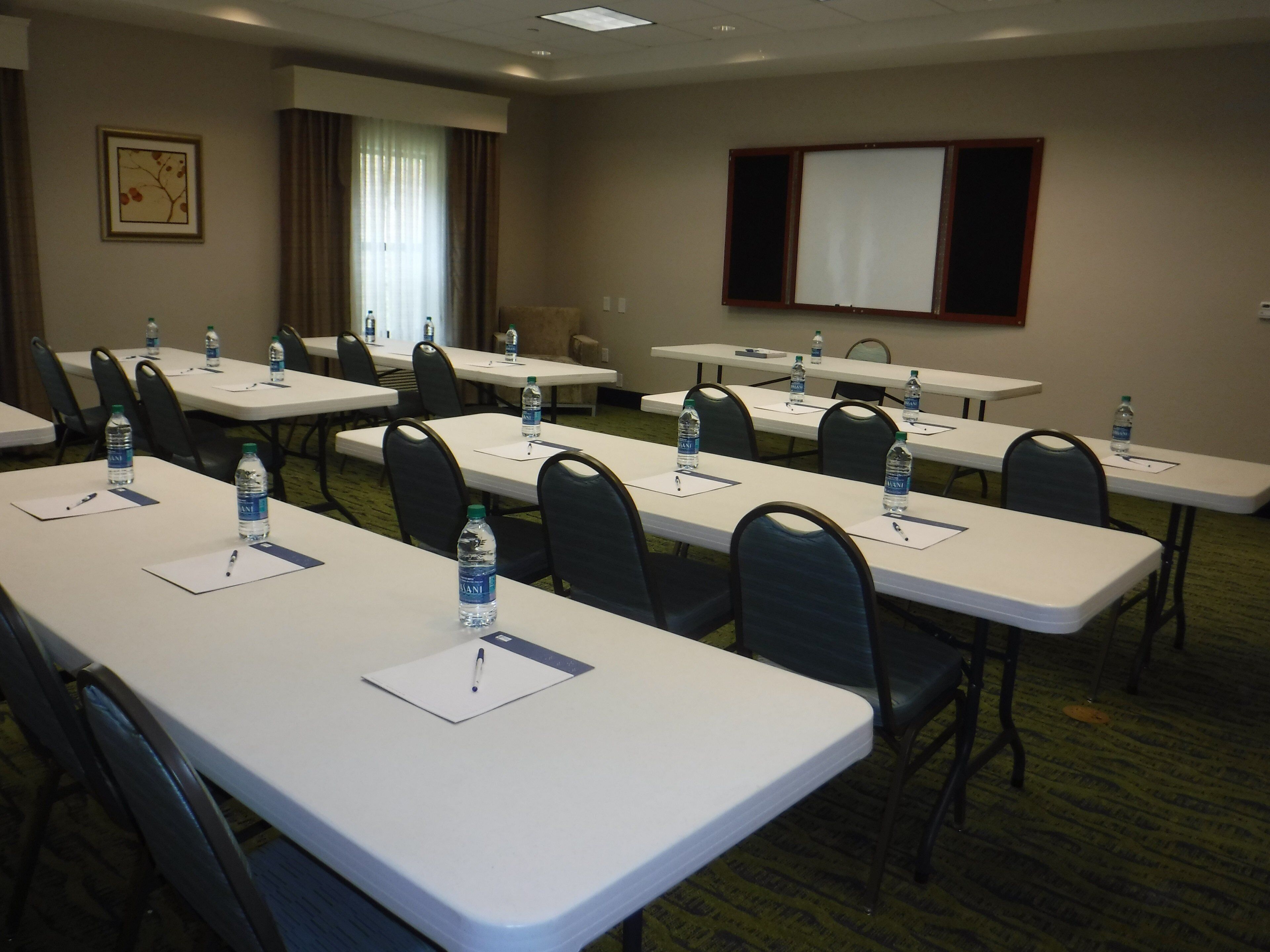 A conference room with multiple tables, chairs, water bottles, and a projector screen.