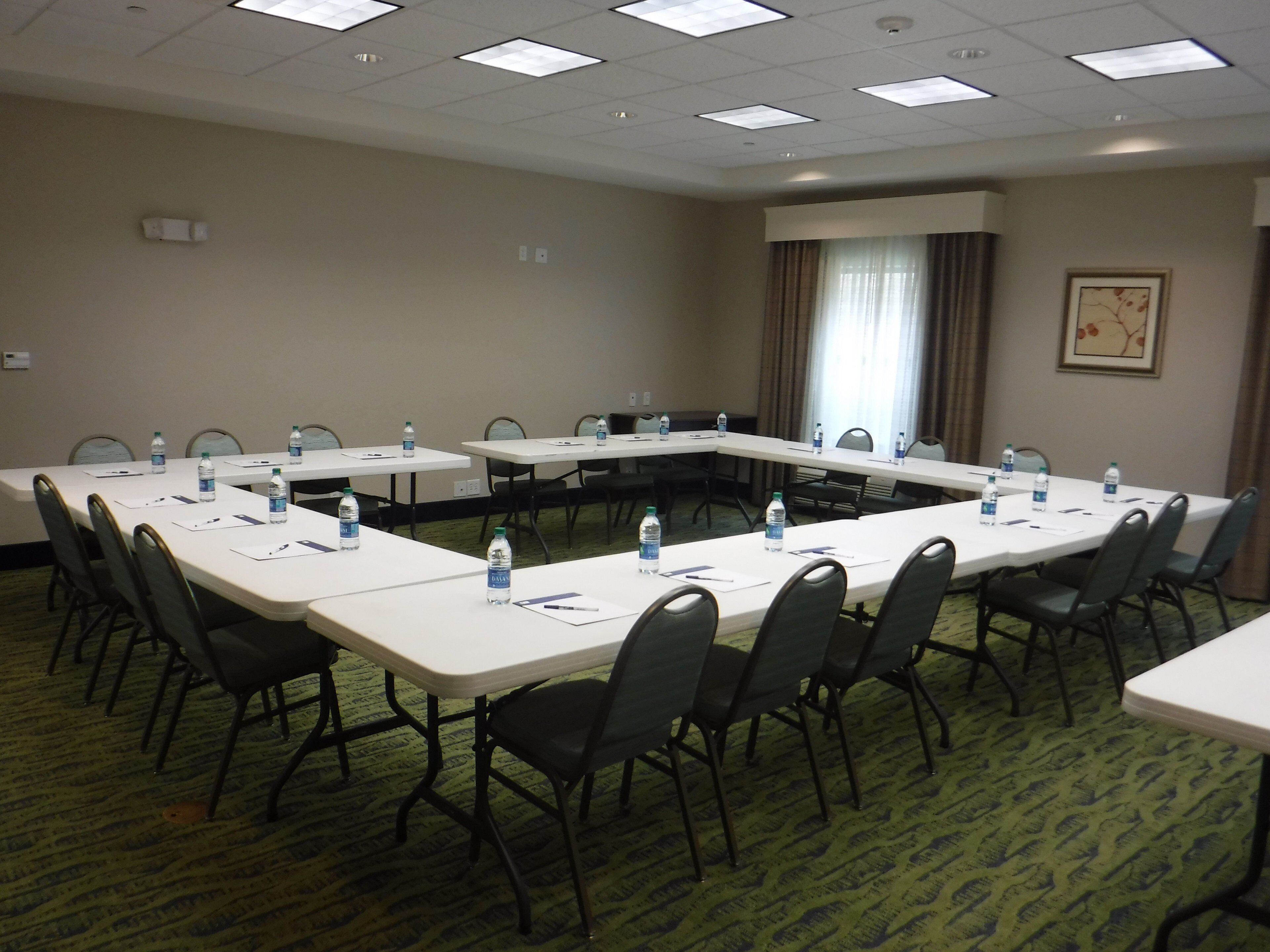 A conference room with long tables, chairs, water bottles, and a carpeted floor.