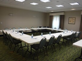 Un salón de conferencias con largas mesas, sillas, botellas de agua y piso alfombrado.