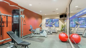 A gym with exercise equipment, a bench, treadmills, and red exercise balls.