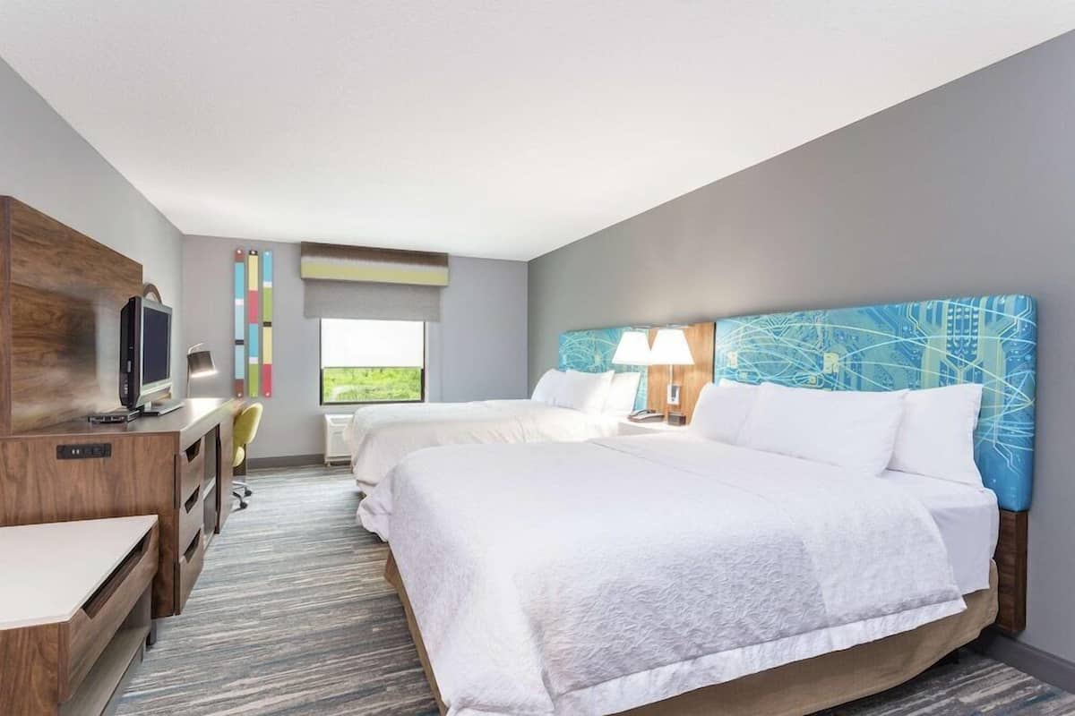 A hotel room with two beds, a desk, a TV, and a window with a view.