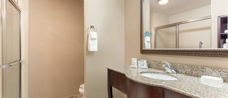 A bathroom with a granite countertop sink, a large mirror, and a glass shower enclosure.