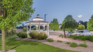 A gazebo with a white roof and open sides, surrounded by a well-maintained lawn and shrubs.