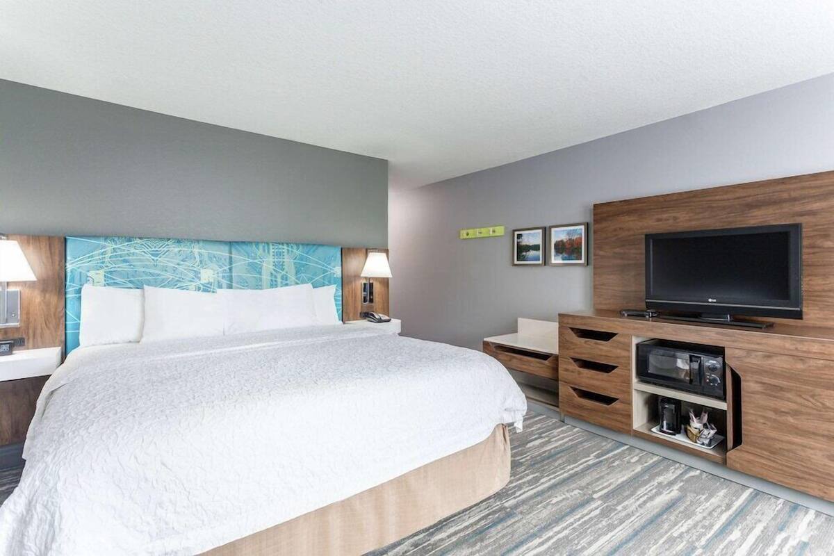 A hotel room with a bed, a TV, a desk, and a wall-mounted shelf.