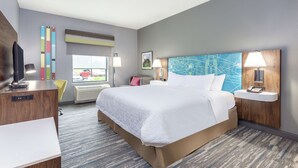 A modern hotel room with a large bed, a desk, a chair, a TV, a window with a view, and a map artwork on the wall.