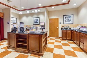 A hotel kitchen with a checkered floor, a coffee station, and a door leading to another room.