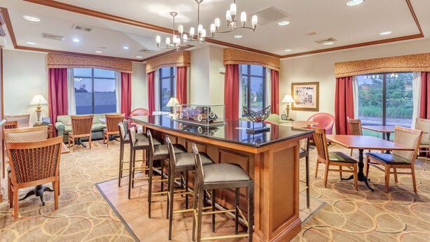 A hotel lobby with a bar area, seating arrangements, and large windows with curtains.