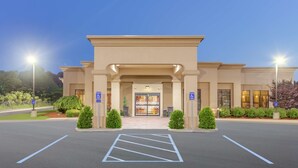A hotel entrance with a parking lot, handicap accessibility signs, and a well-lit facade.