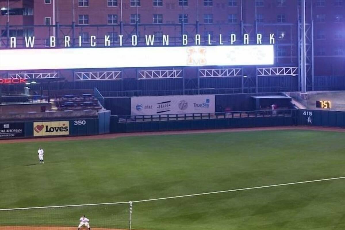 Ein Hotel mit einem Schild, auf dem 'Harlem Inn & Suites' steht, und einem großen, beleuchteten Schild über dem Feld mit der Aufschrift 'Raw Bricktown Ballpark'.