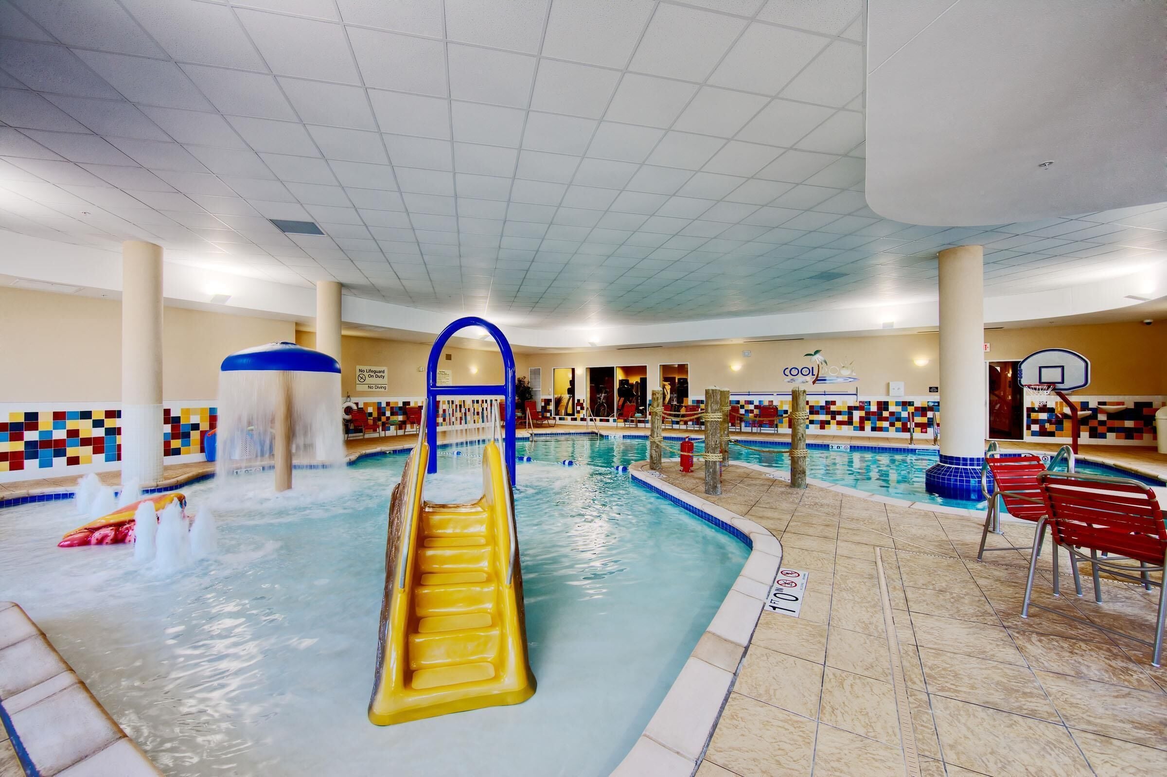 An indoor swimming pool with a water slide, multiple lanes, and a basketball court.