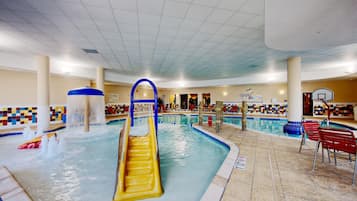 An indoor swimming pool with a water slide, multiple lanes, and a basketball court.