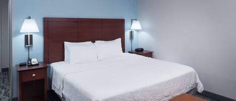 A hotel room with a large bed, two bedside tables with lamps, a telephone, and a brown ottoman.