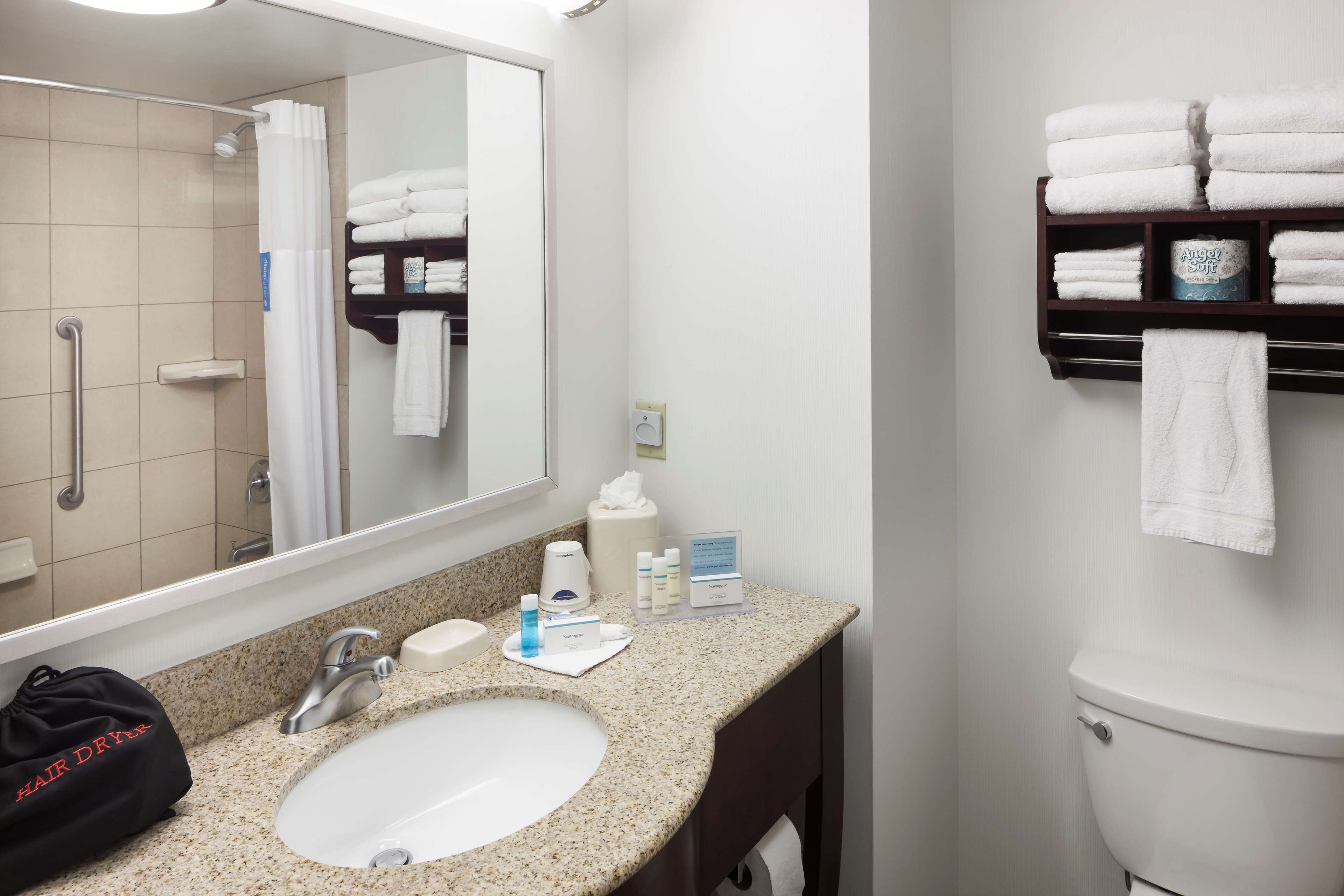 A hotel bathroom with a granite sink, a mirror, a towel rack, and a toilet.