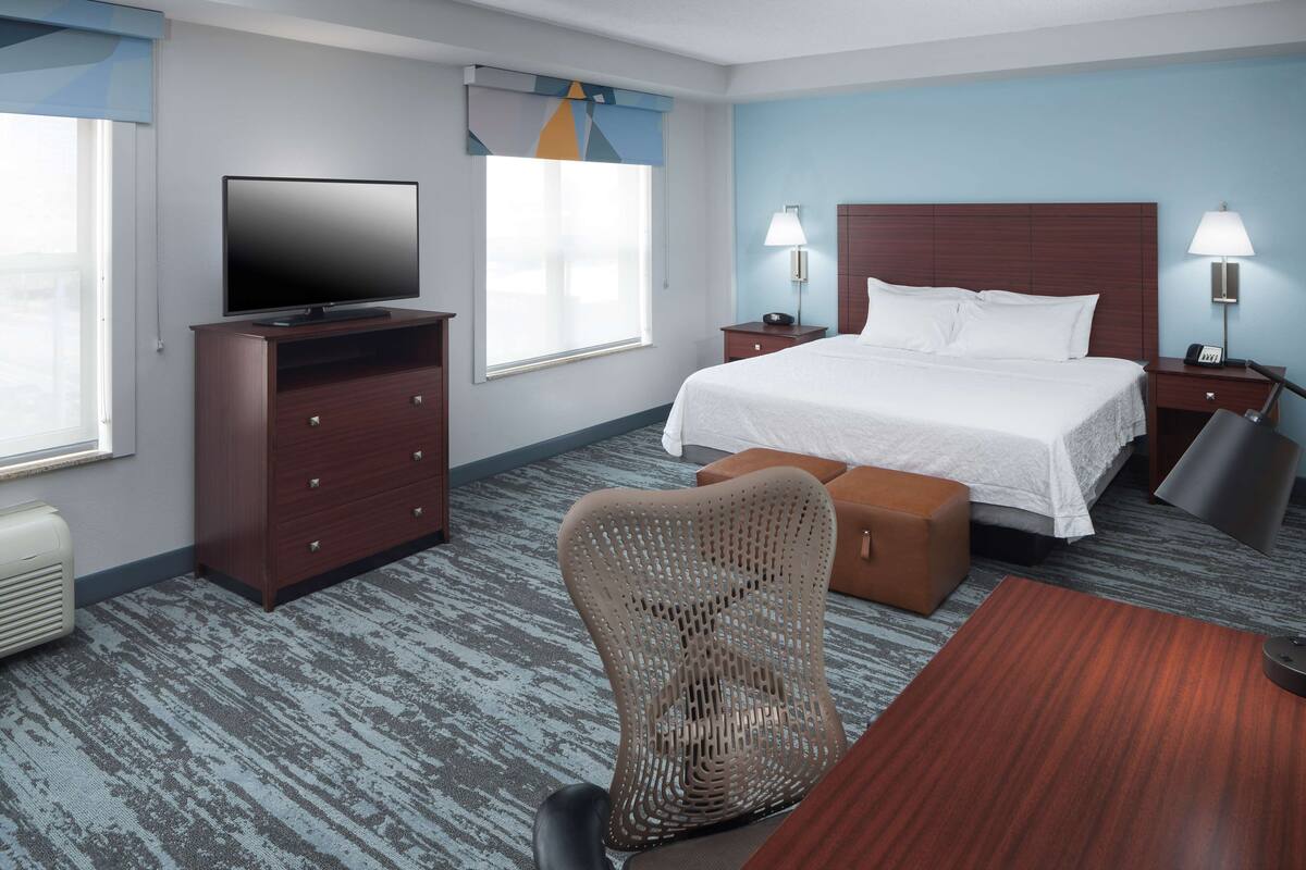 Ein Hotelzimmer mit Bett, Fernseher, Schreibtisch, Stuhl und Nachttisch mit Lampen.