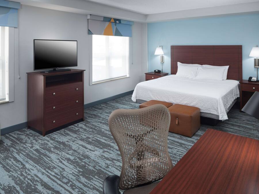 A hotel room with a bed, a TV, a desk, a chair, and a nightstand with lamps.