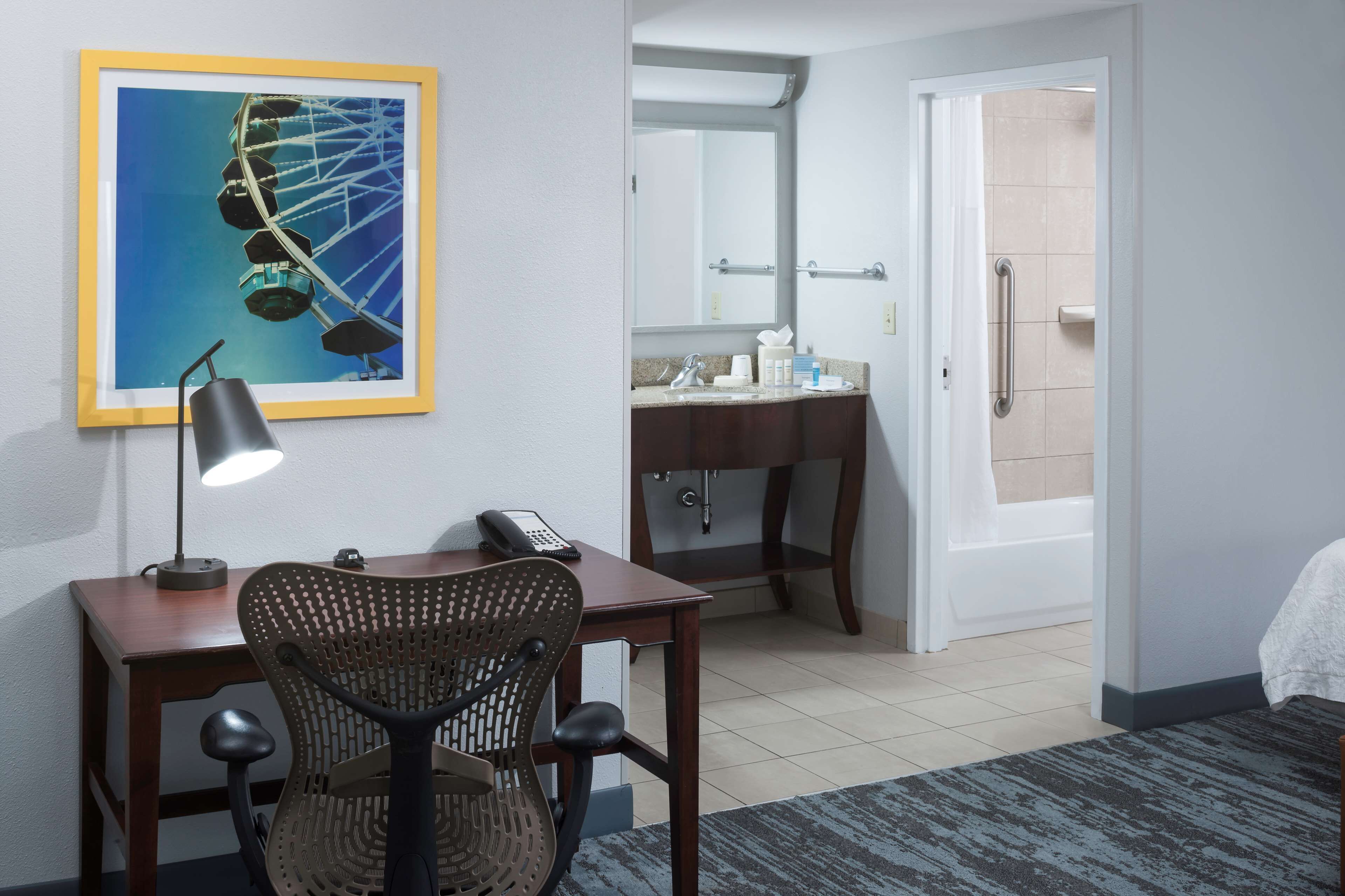 A hotel room with a desk, chair, and a large mirror.