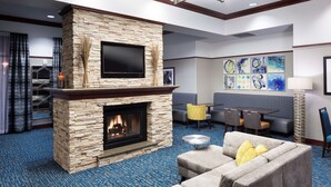 A hotel lobby with a stone fireplace, a flat-screen TV, a sofa, and a dining area.