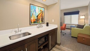 A modern hotel room with a kitchenette, a large window with a view, a sofa, and a lamp. - Hampton Inn & Suites by Hilton Walla Walla (Walla Walla)