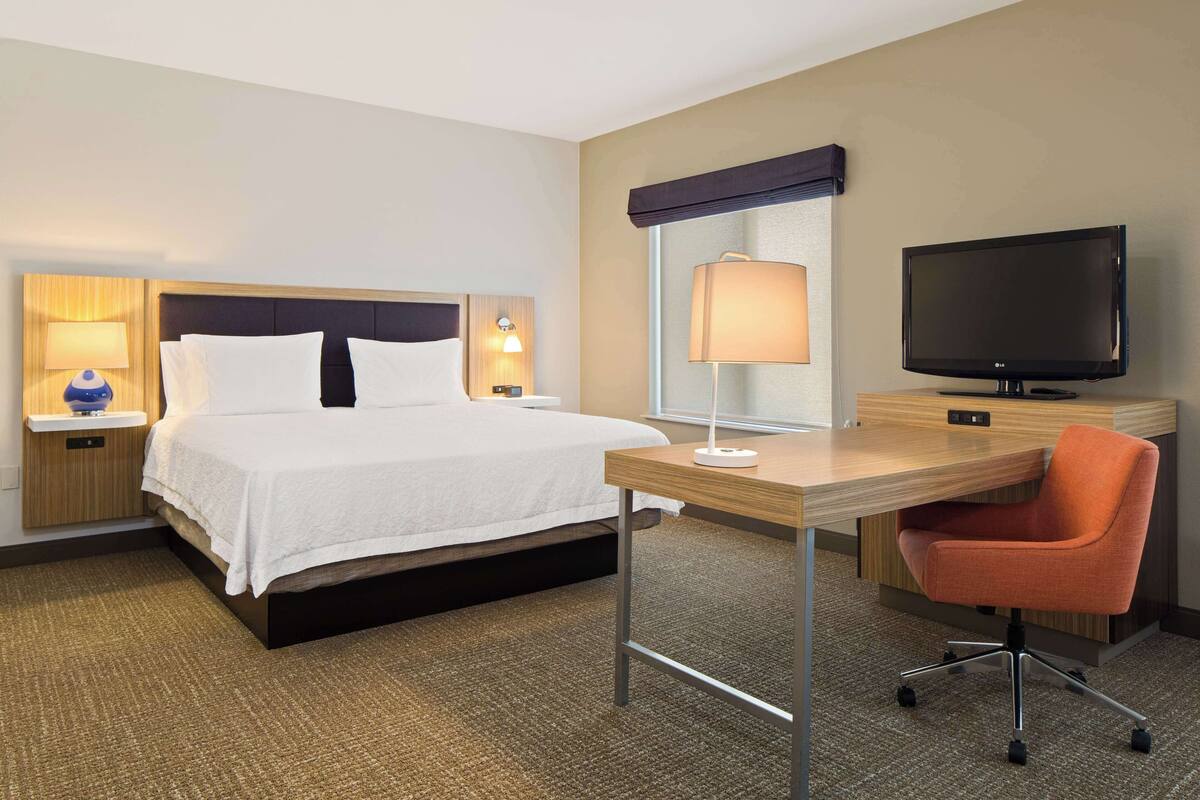 A hotel room with a bed, a desk, a chair, a television, and two lamps.