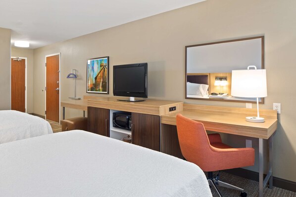 Habitación de hotel con dos camas, un escritorio, televisor, silla, lámpara y microondas.
