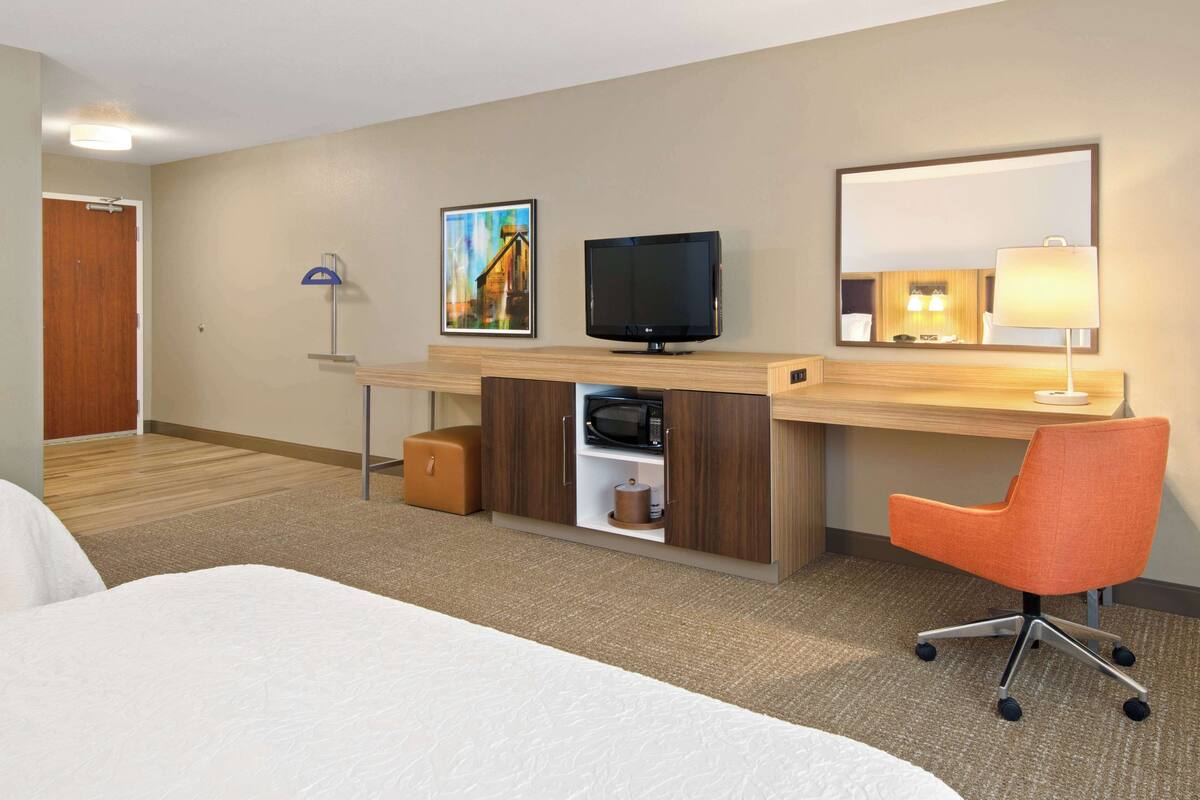 A hotel room with a bed, a desk with a computer, a television, a lamp, and a painting on the wall.