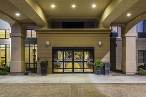 Entrada de hotel con puertas dobles, suelo de baldosas y plantas en macetas.