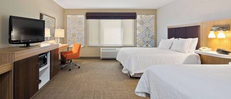 A hotel room with two beds, a desk with a TV, a chair, and a window with patterned curtains.