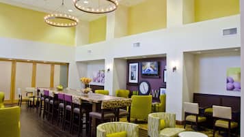 A hotel dining area with a long table, multiple chairs, and a chandelier.