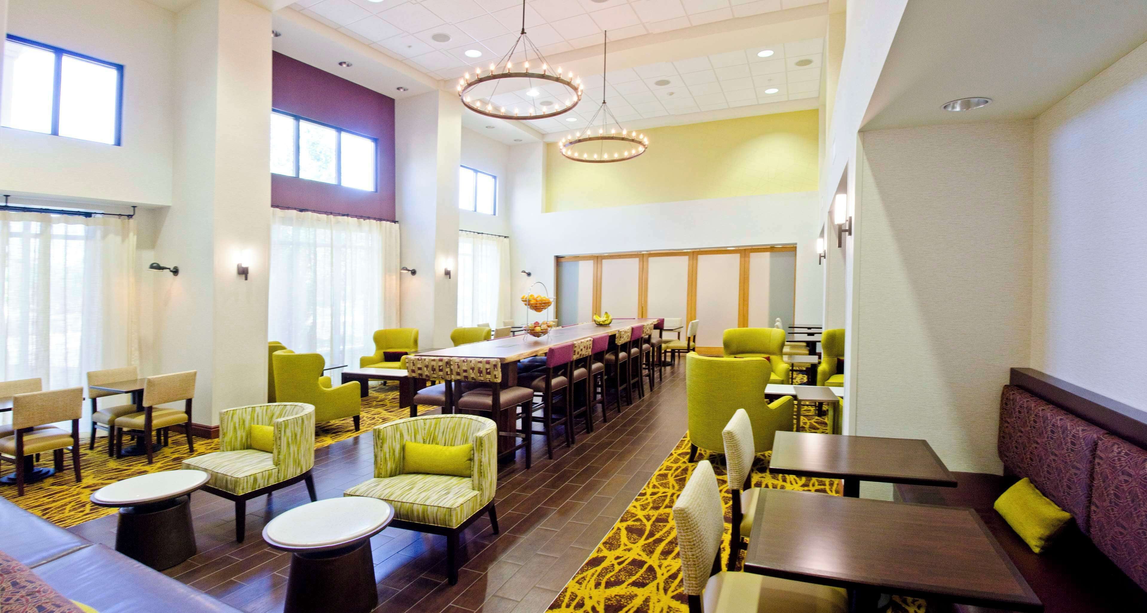 A spacious dining area with high tables and chairs, large windows, and a yellow patterned carpet.