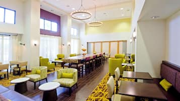 A spacious dining area with high tables and chairs, large windows, and a yellow patterned carpet.