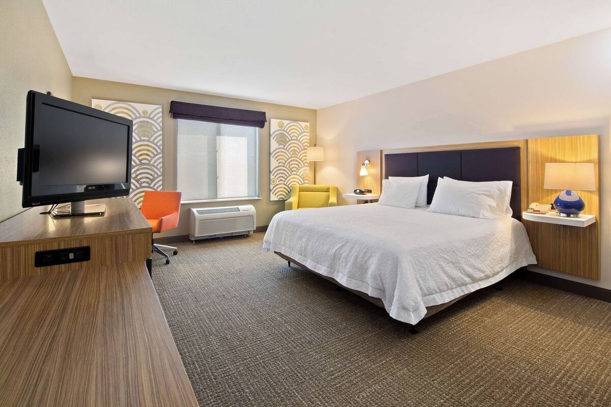 A hotel room with a bed, a television, a desk, and a chair.
