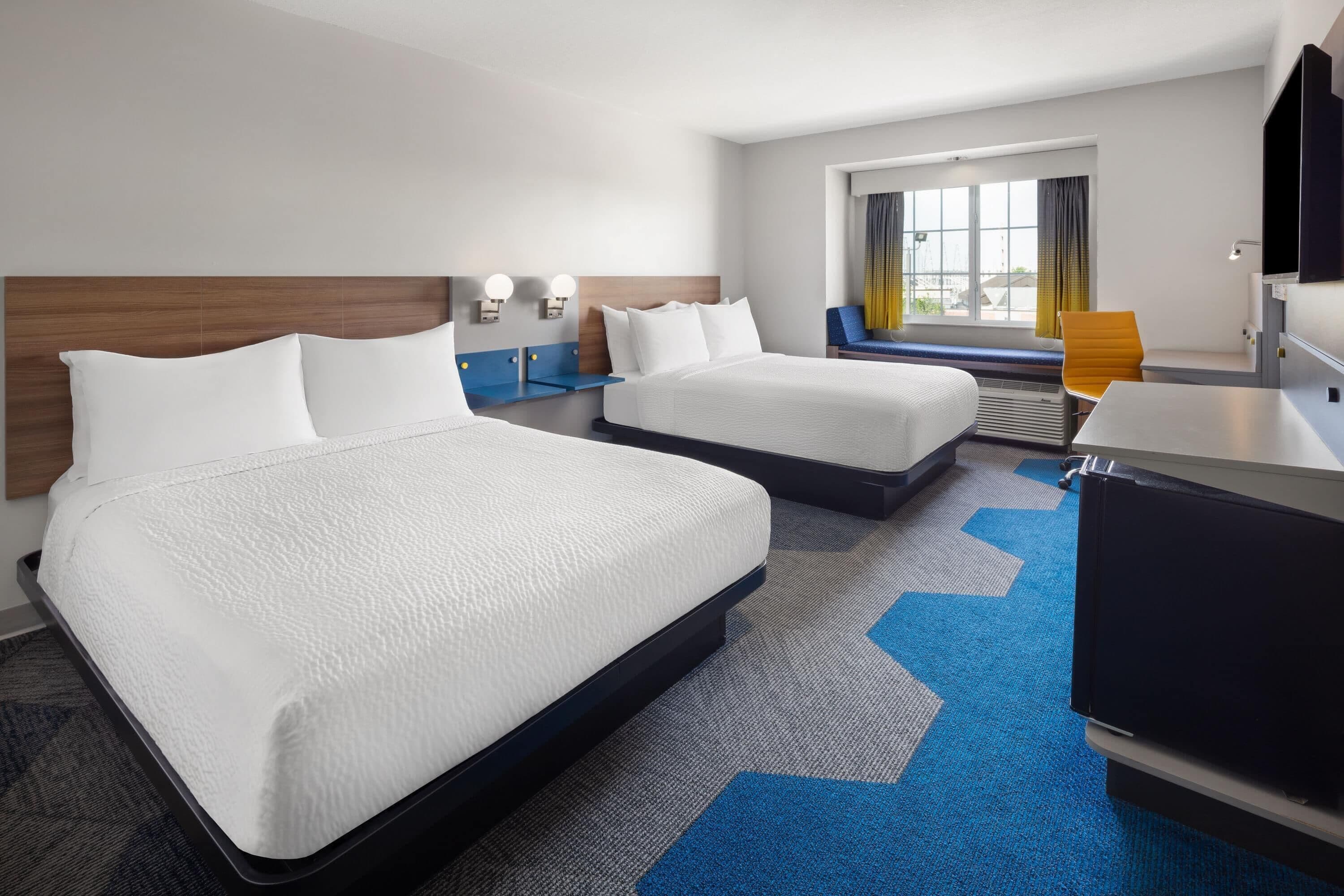 A hotel room with two beds, a desk, a chair, a TV, and a window with curtains.
