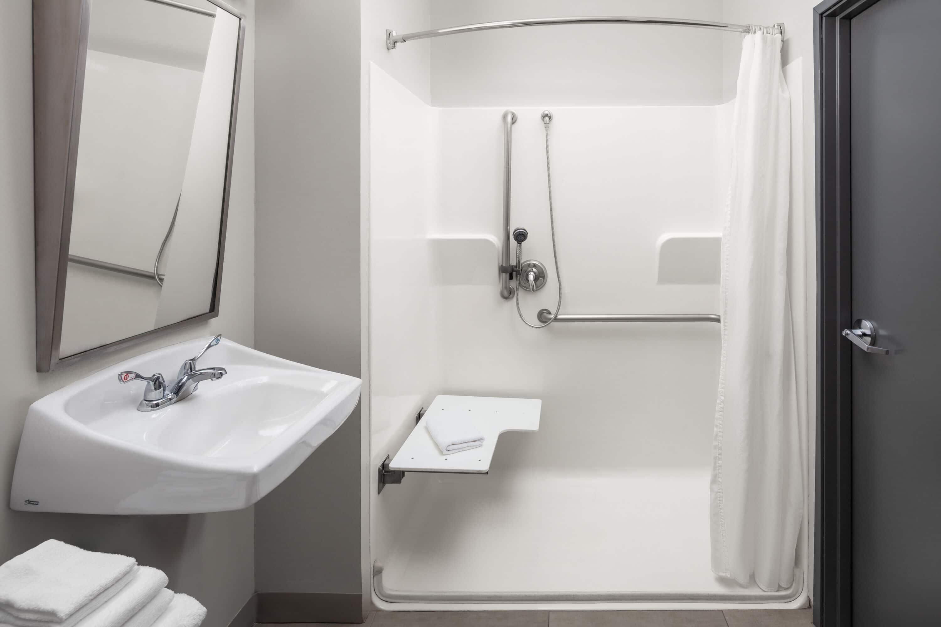Een badkamer met een wastafel, spiegel, douche en handdoekhouder.