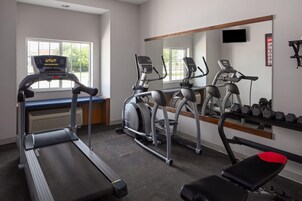 Un gimnasio con cintas de correr, elípticas, una banca y un espejo.