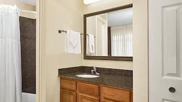 A bathroom with a granite countertop sink, wooden cabinets, a large mirror, and a white shower curtain.