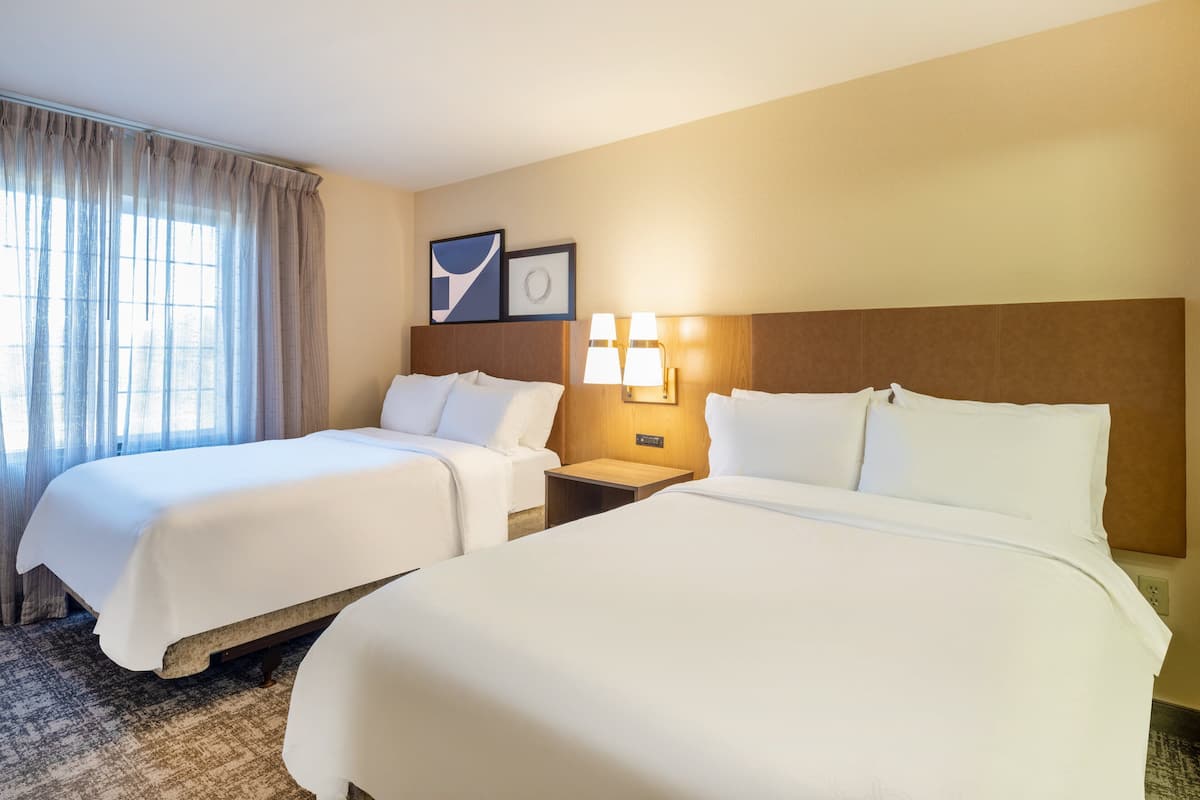 Une chambre d’hôtel avec deux lits, une table de chevet, une lampe et une fenêtre avec des rideaux.