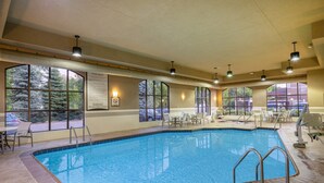 Une piscine intérieure avec des règles d’utilisation clairement affichées, un panneau indiquant la présence d’un sauveteur et une vue sur l’extérieur grâce à de grandes fenêtres.