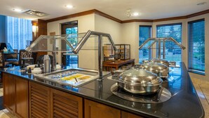 A buffet area with a glass enclosure, stainless steel serving dishes, and a coffee station. - Staybridge Suites Milwaukee Airport South by IHG (Franklin)