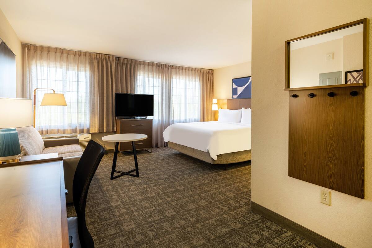 Une chambre d’hôtel comprenant un lit, une télévision, un bureau avec une chaise, une petite table et un miroir.