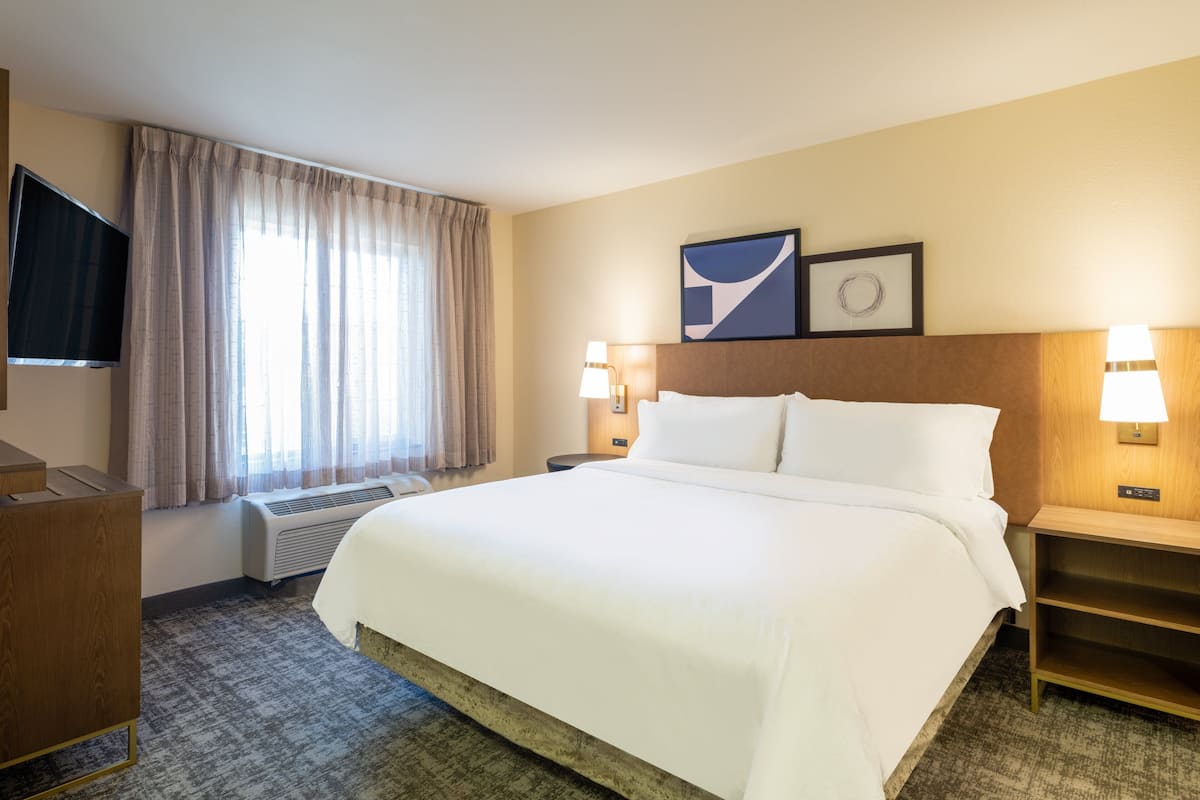 Une chambre d’hôtel avec un grand lit, un téléviseur à écran plat, un bureau et une fenêtre avec des rideaux.