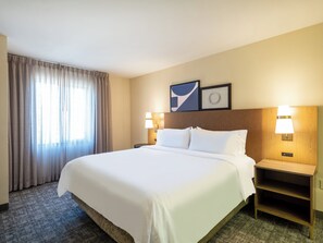 Een hotelkamer met een groot bed, twee bedlampjes, een nachtkastje, een vloerbedekking en een raam met gordijnen.
